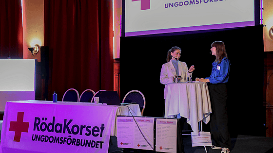 Två personer står och presenterar på Röda Korsets Ungdomsförbunds riksårsmöte.